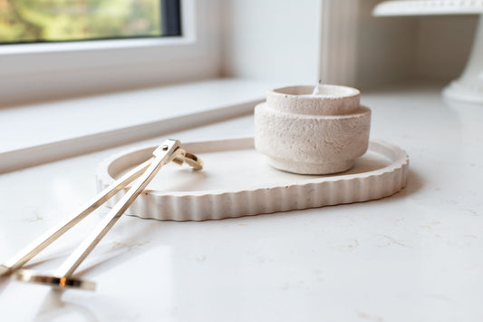 Oval Limestone tray on marble surface with a gold candle wick cutter. Limestone candle on the tray