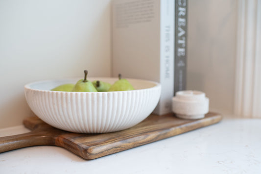 Limestone bowl with pears on a wooden tray against a neutral background