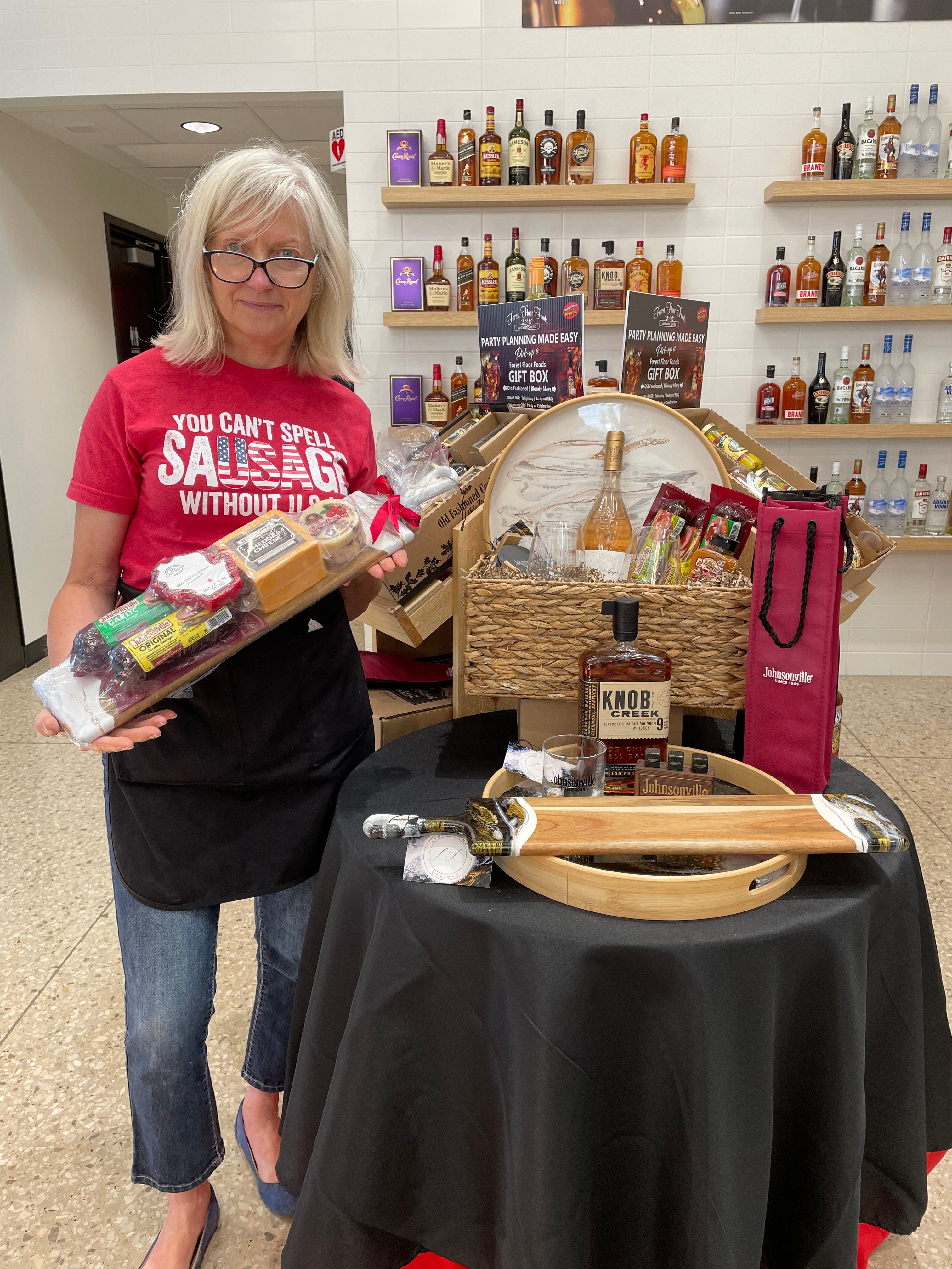 A Johnsonville Owner Holding A Lynn & Liana Charcuterie Board around other Lynn & Liana Designs Serving Trays in baskets.
