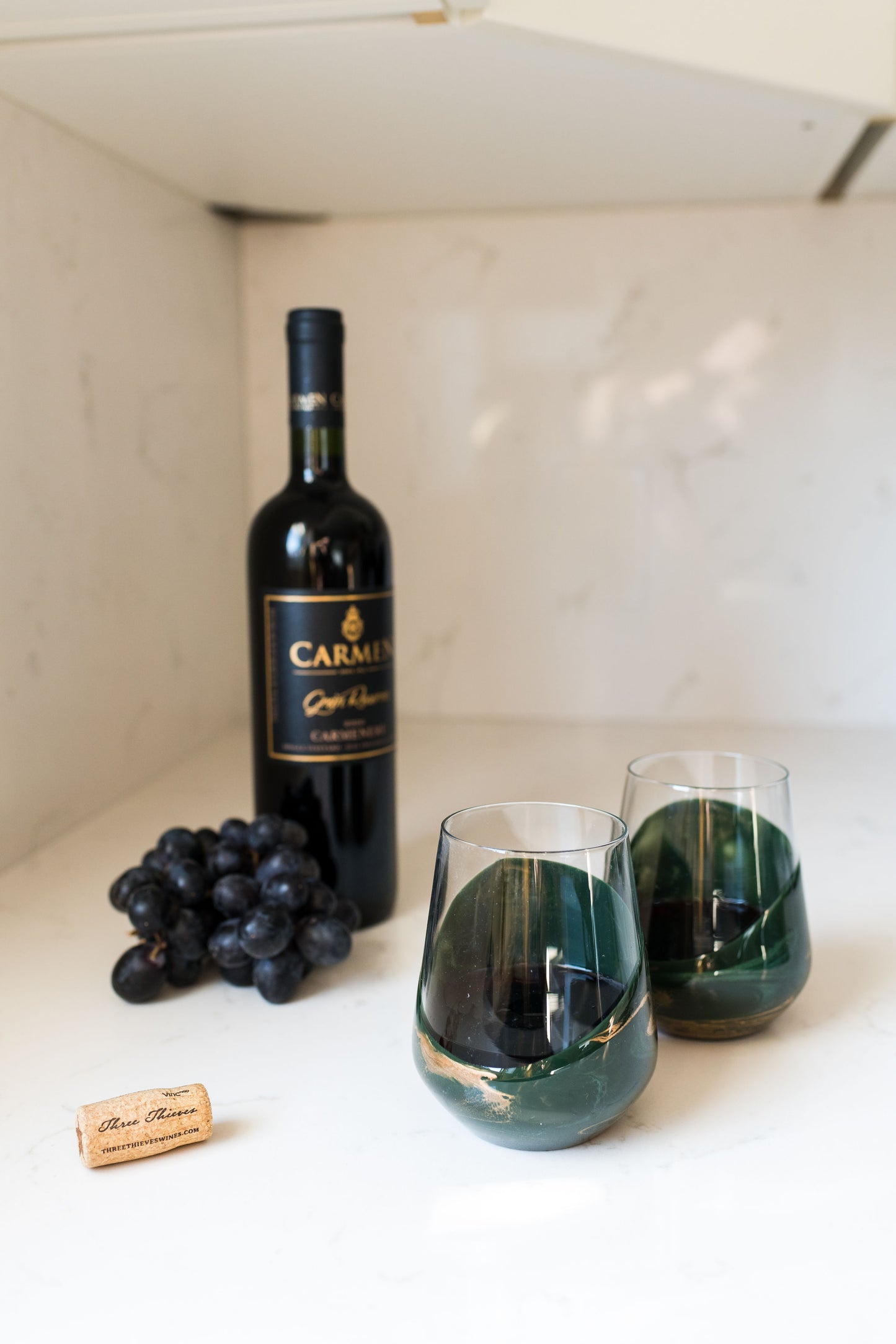 Jade wine glasses on kitchen counter with grapes and wine bottle