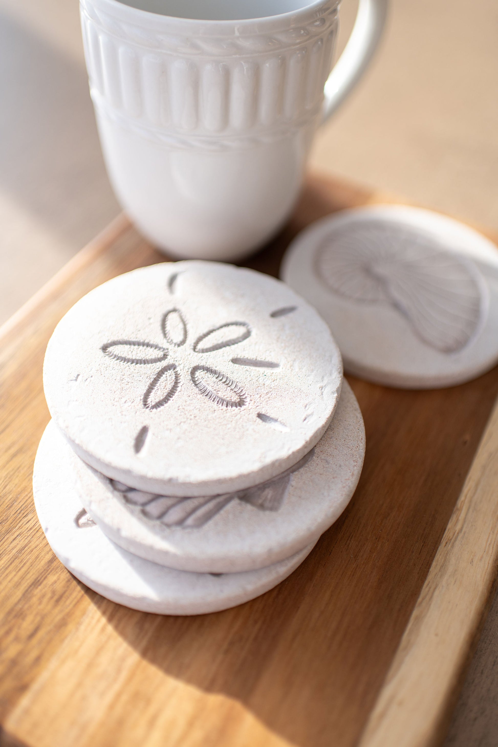 White ceramic coasters with coastal design on a wooden surface next to a white mug.