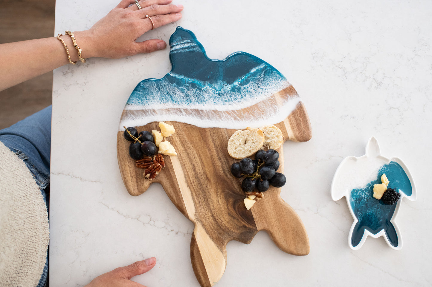 Wooden cutting board shaped like a turtle with Ocean blue resin , placed on a white surface with the matching small ceramic turtle tray 