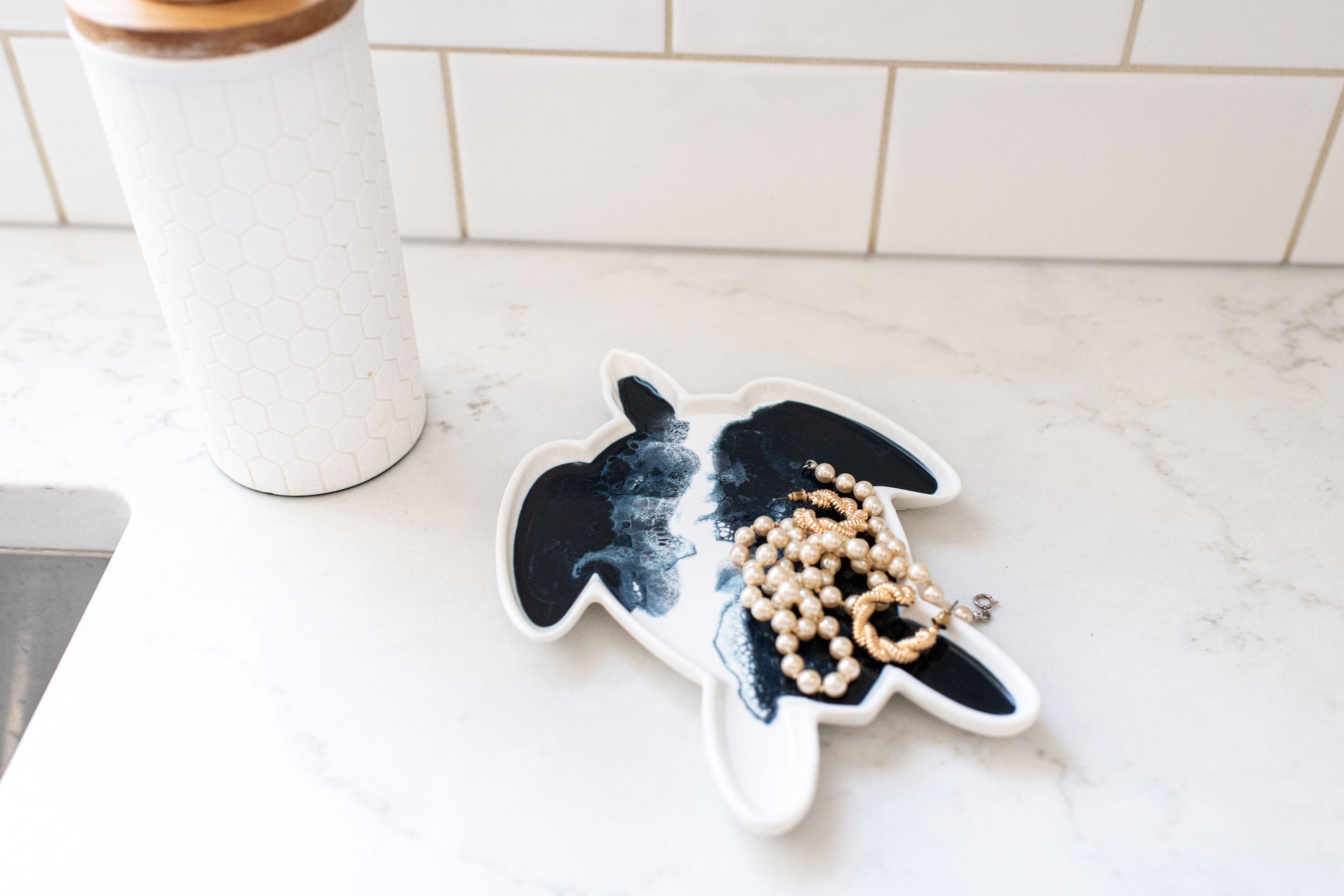 Navy white metallic turtle ceramic tray on a kitchen counter decorated with some gold jewelry 