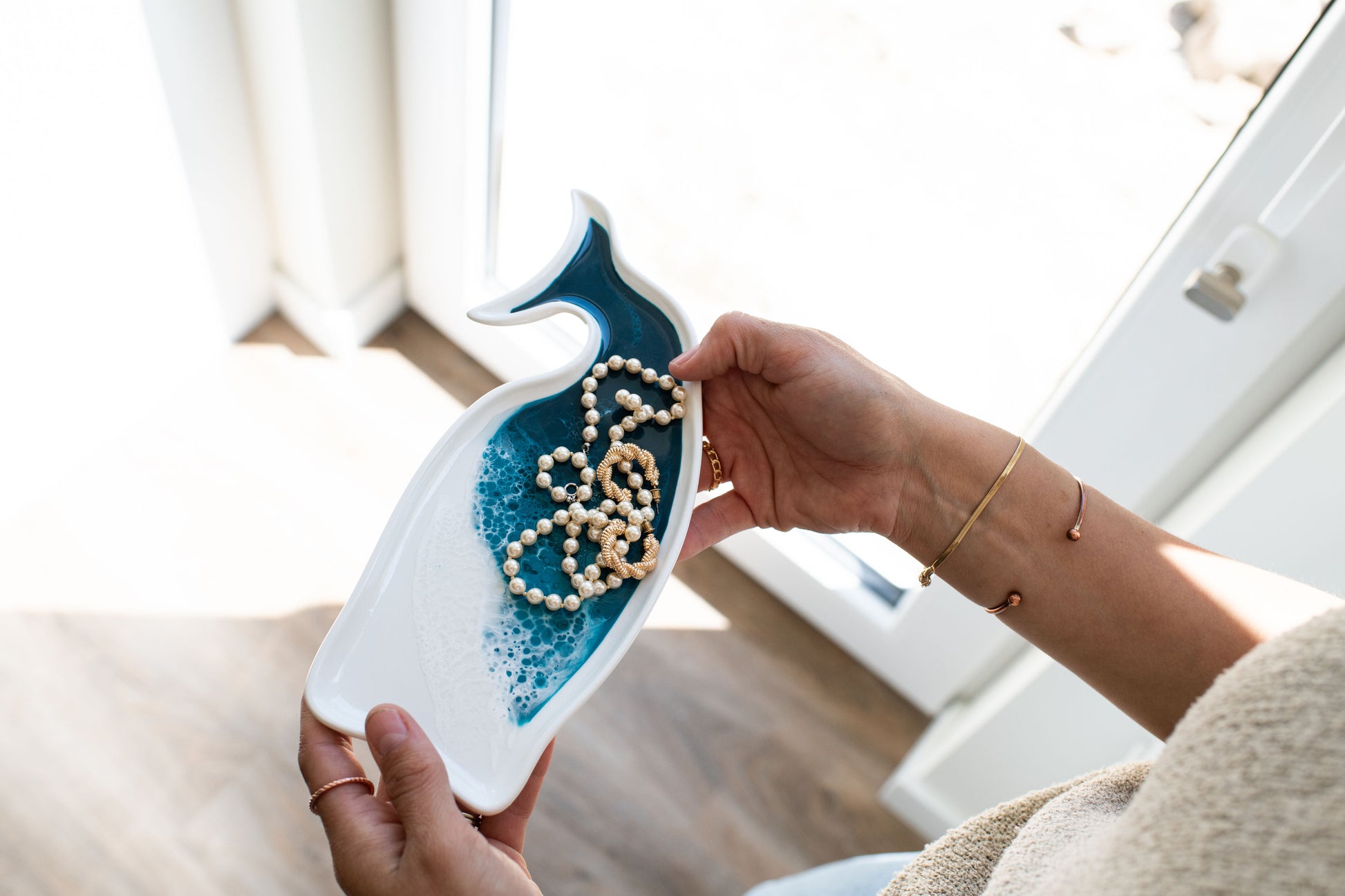 hands holding the ocean vibes whale ceramic tray displaying golf jewelry on it 