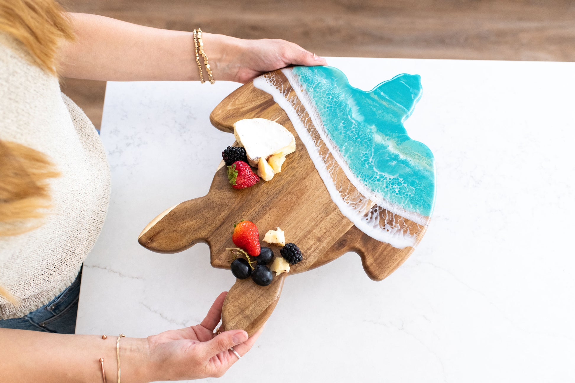 Wooden turtle-shaped cutting board with Caribbean blue resin  design, held by a person.