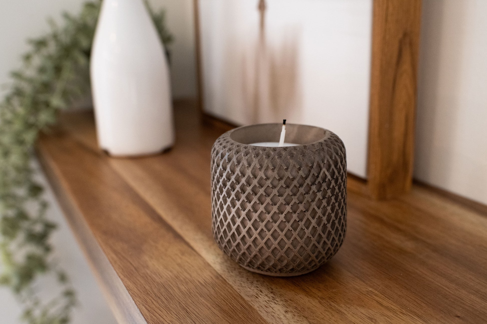 mocha stone candle holder with a lit candle on a wooden shelf.