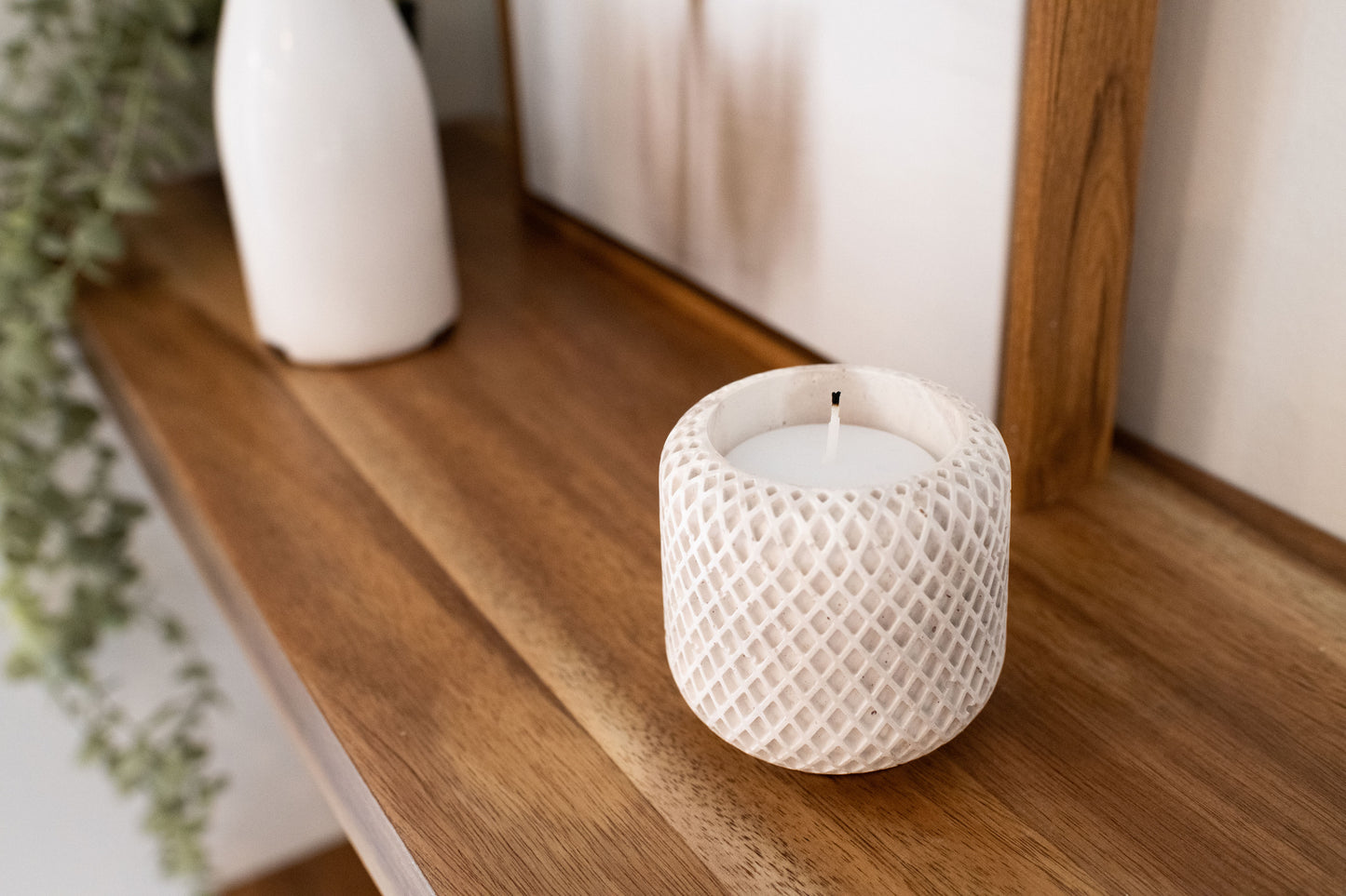 limestone textured lattice vessel, candle holder with a candle on a wooden shelf.