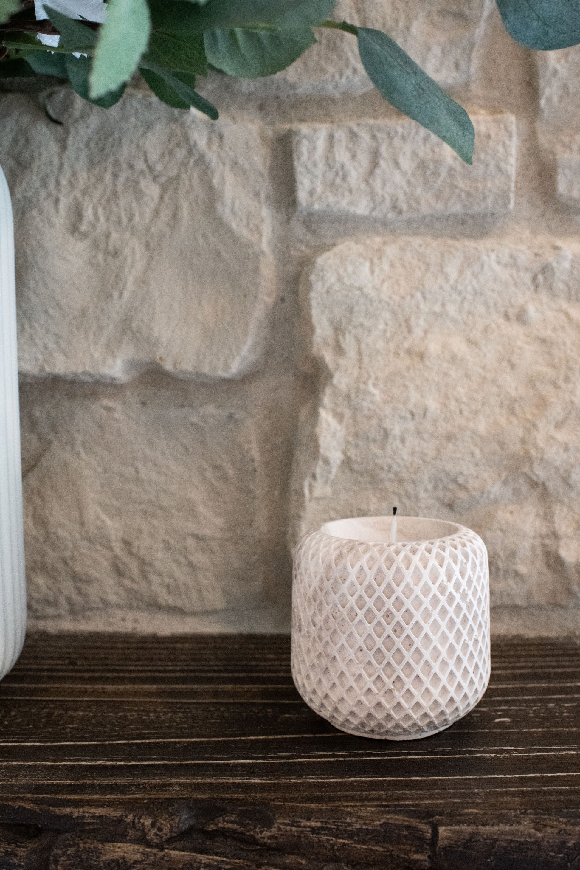 Limestone candle holder on a wooden surface with a stone wall background