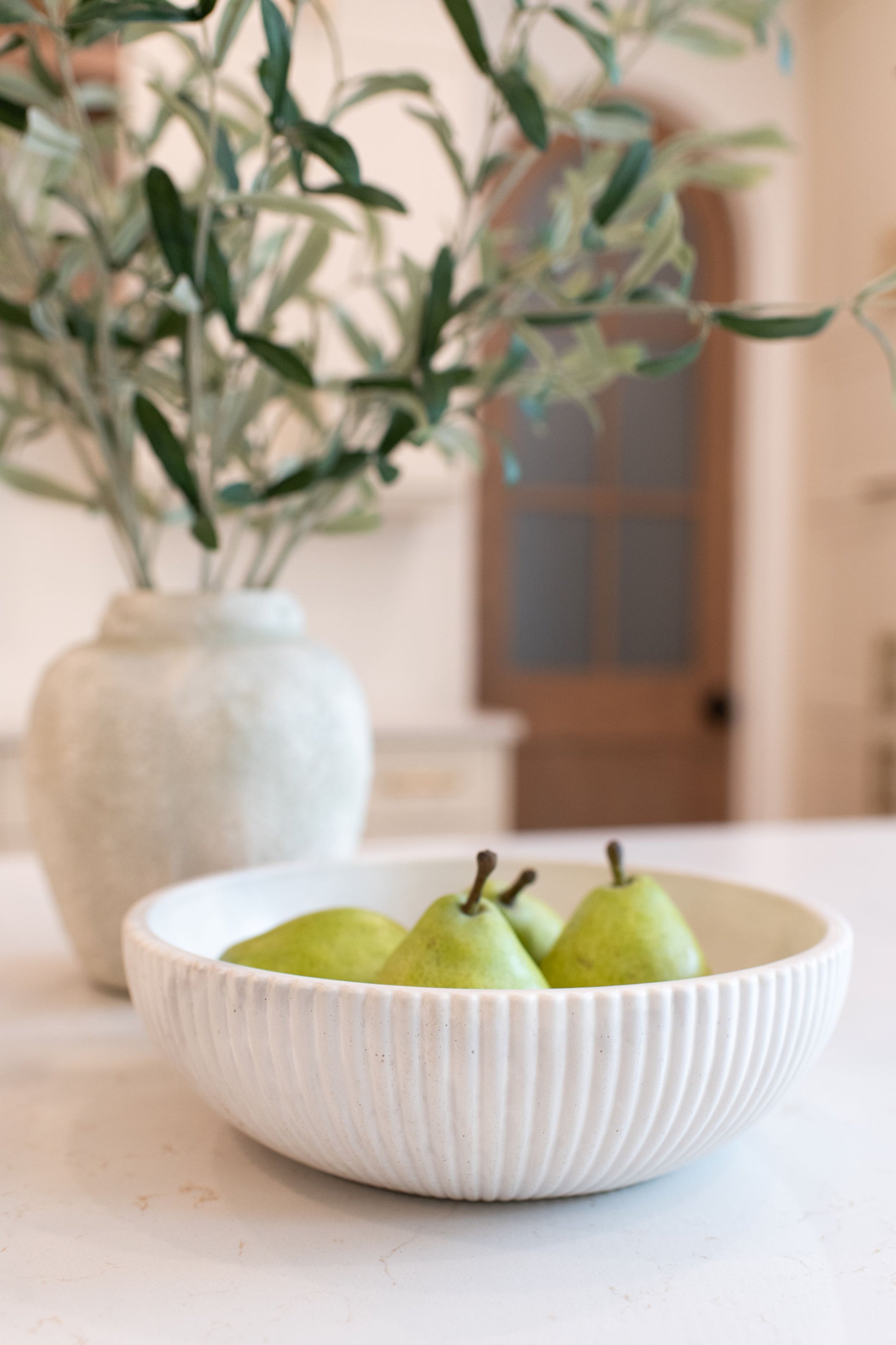 Limestone bowl with pears on a table next to a vase with greenery