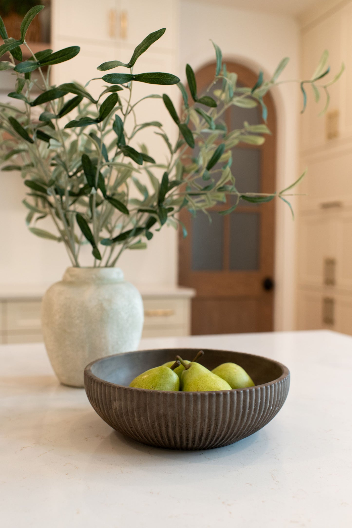 Mocha stone bowl with pears on a kitchen counter next to a vase with greenery