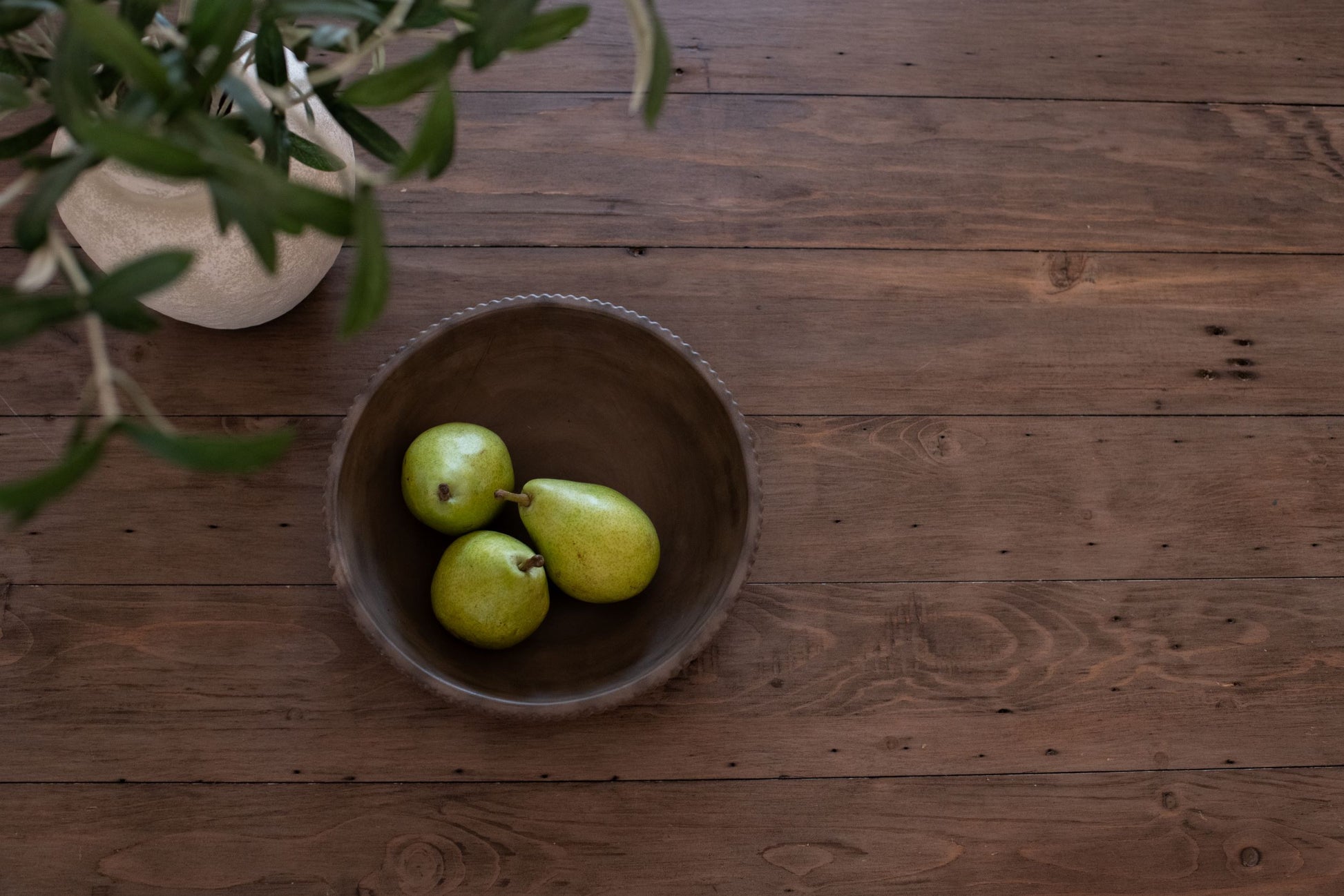 Three green pears in our mocha stone bowl on a wooden surface with an olive branch.