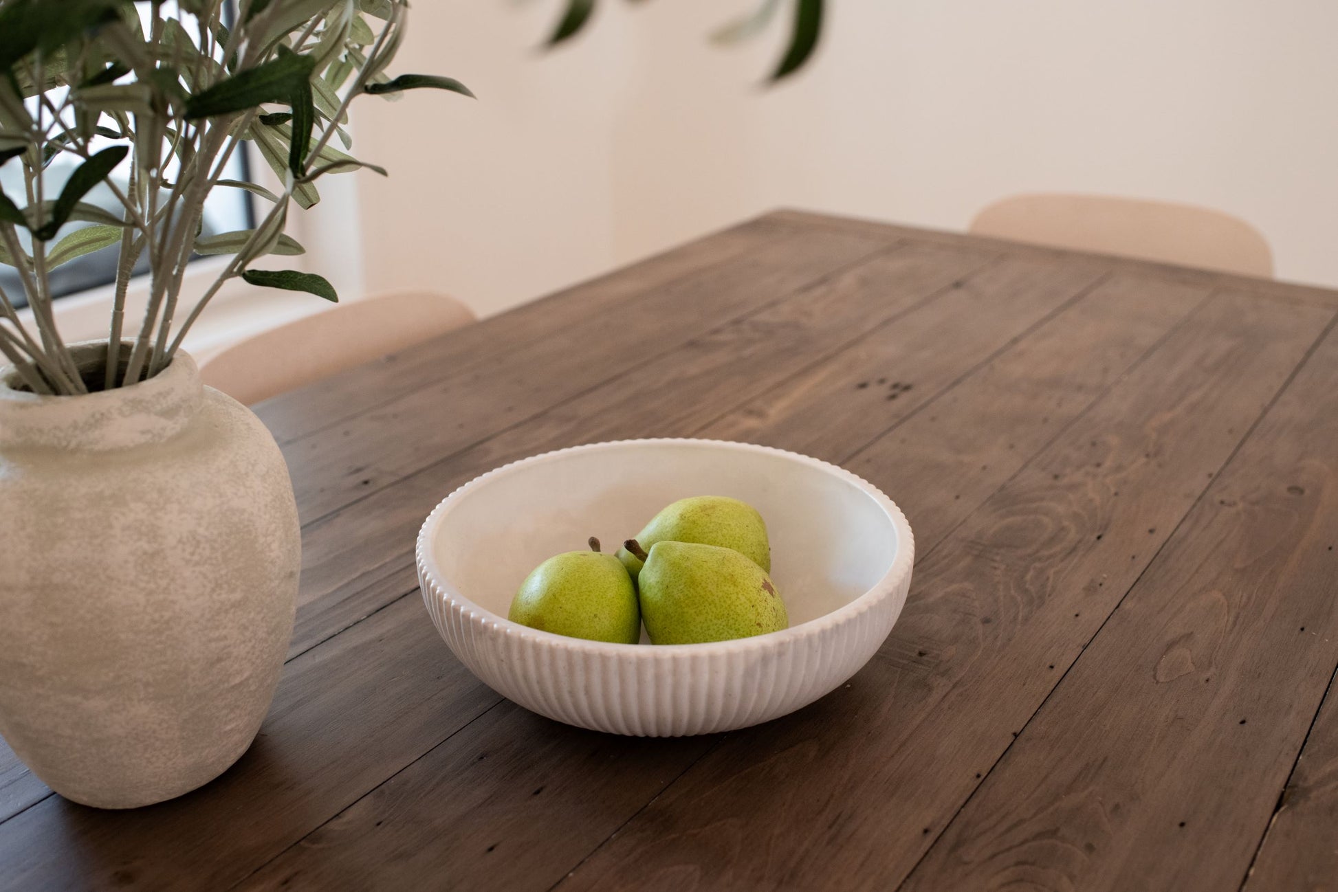Limestone Bowl of pears on a wooden table with a plant in the background