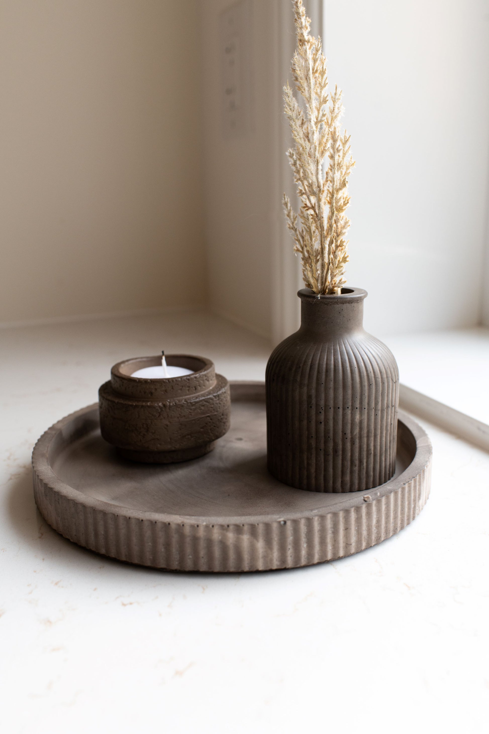 Round mocha tray with bud vase and candle holder on a neutral background.