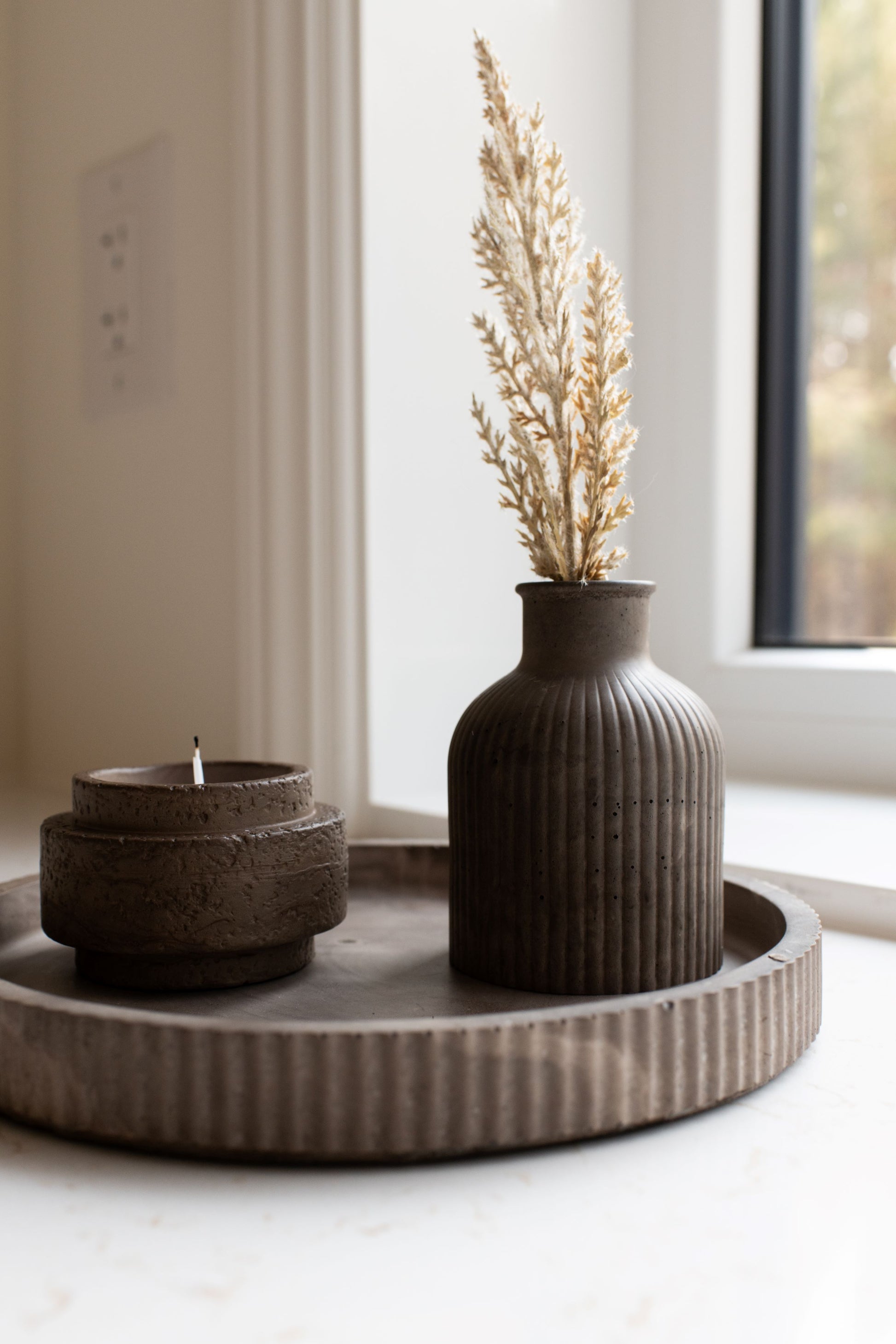 Decorative setting with our mocha round tray and candle holder and bud vase in a home interior.
