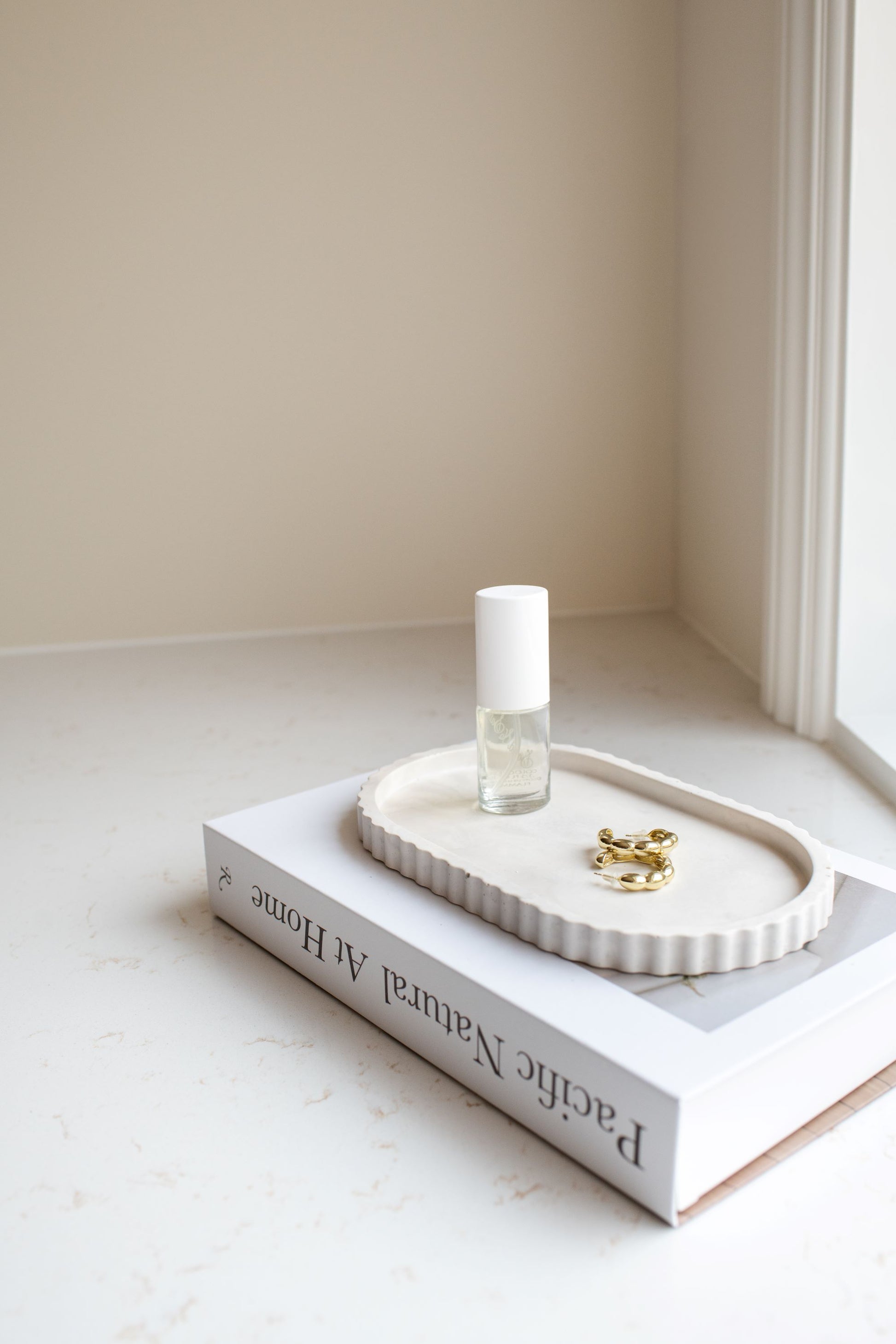 Limestone oval tray with a bottle and jewelry on a book against a neutral wall