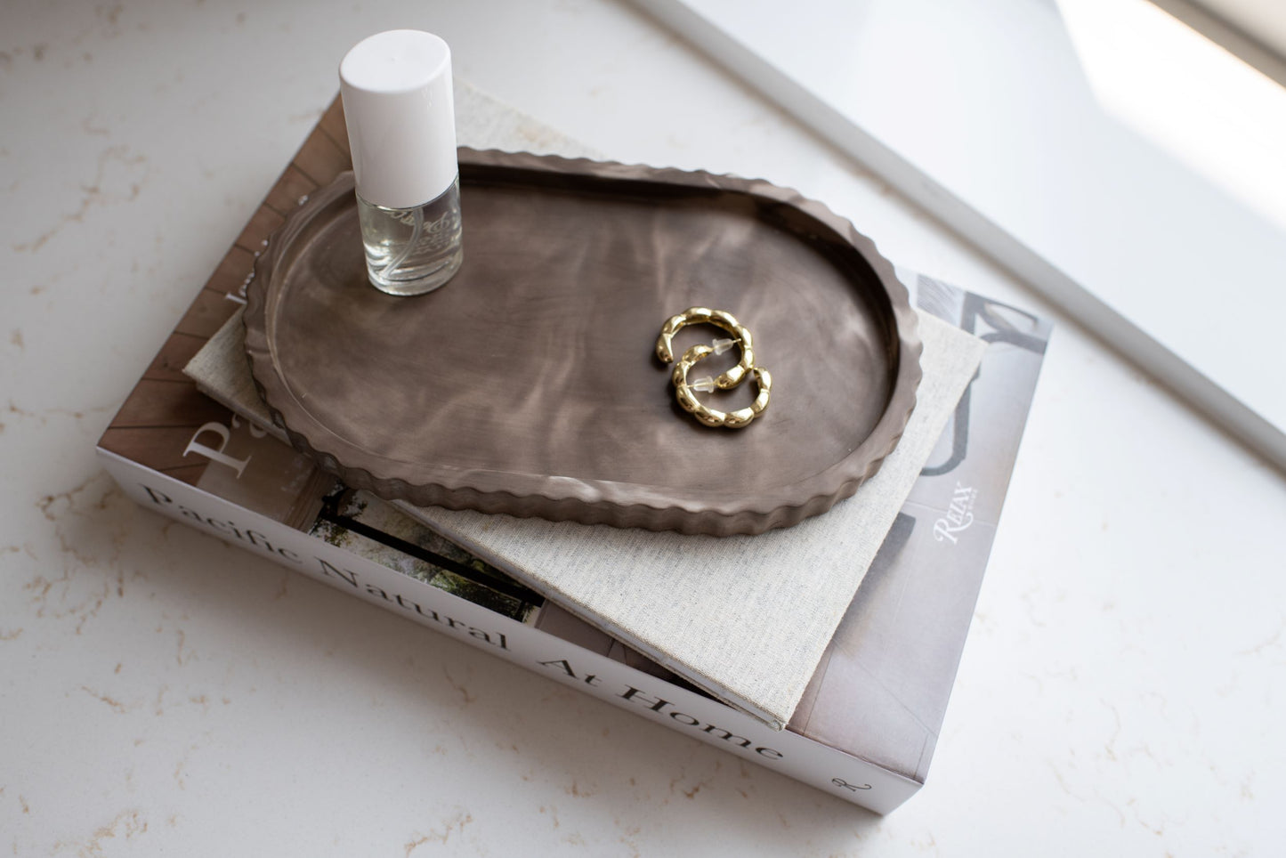 Mocha oval tray with gold earrings and small bottle on a magazine stack 
