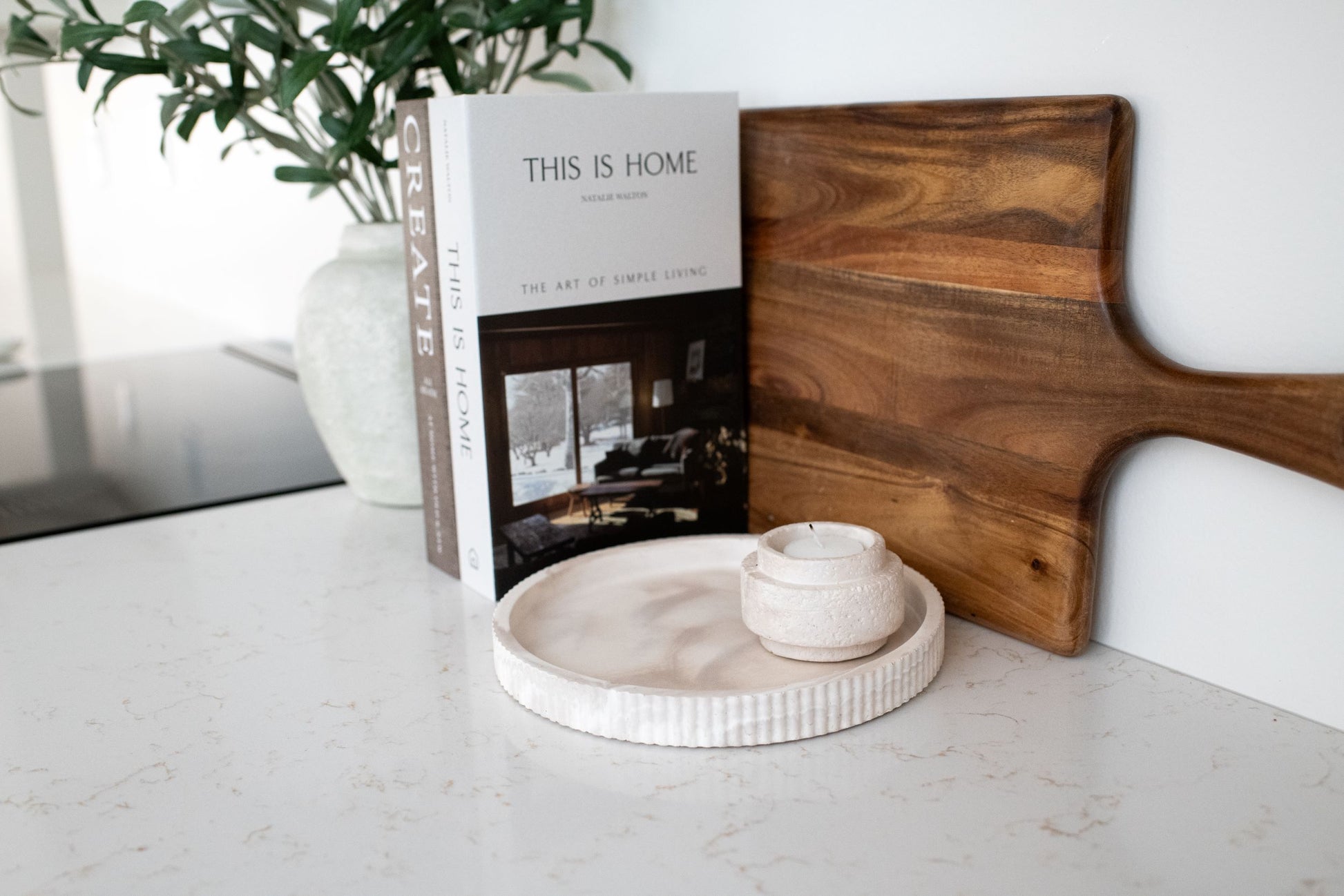 Wooden cutting board,  book titled 'This is Home', with our limestone round tray and candle holder a marble surface.