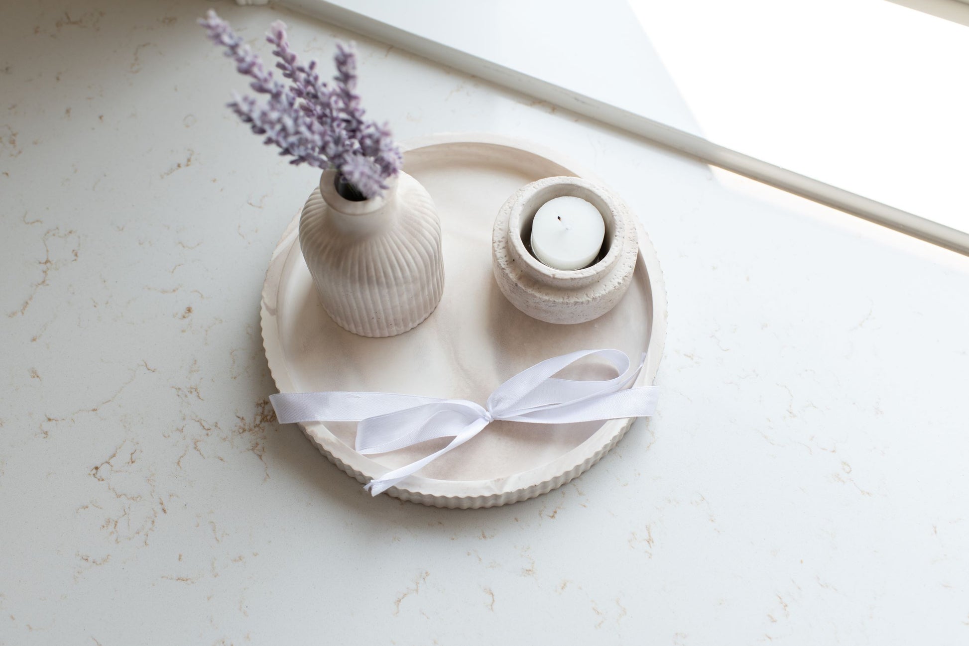 Round limestone tray with the candle holder and budvase decorated on top of it with a white bow 