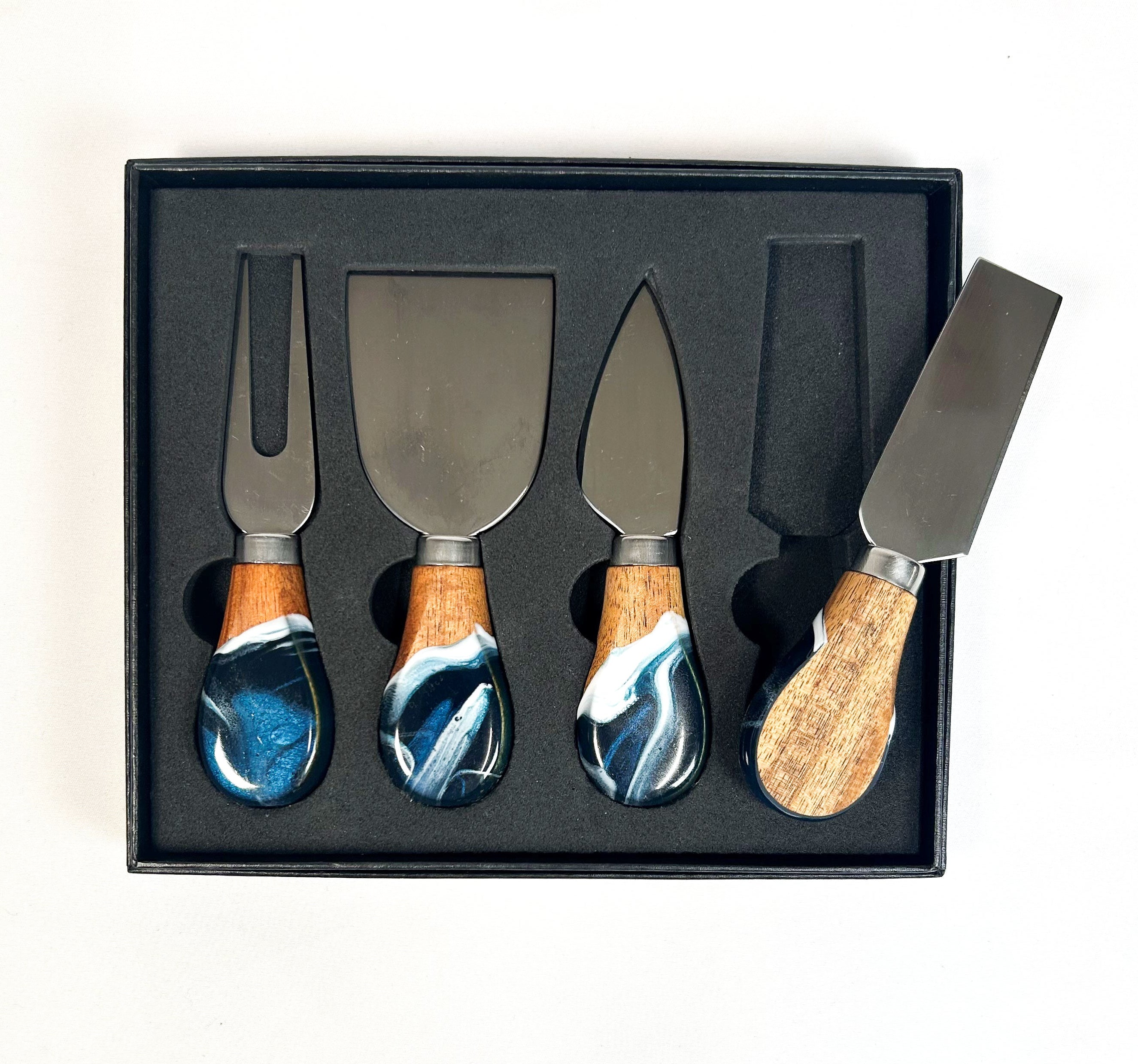 Set of four cheese knives with marbleized wood handles in a black box.