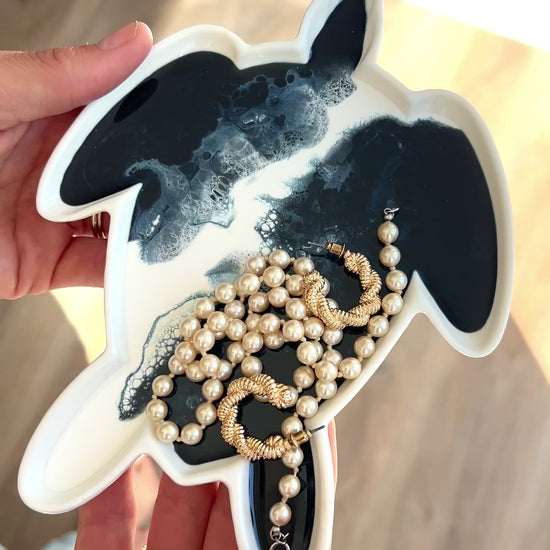 video of a women holding the navy white turtle tray with some jewelry on it 