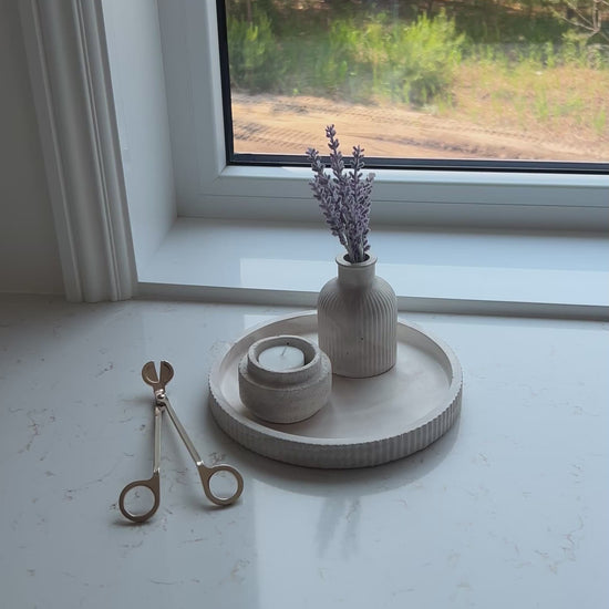Video of our round limestone tray with a candle holder and budvase decorated on a marble countertop in front of a window 