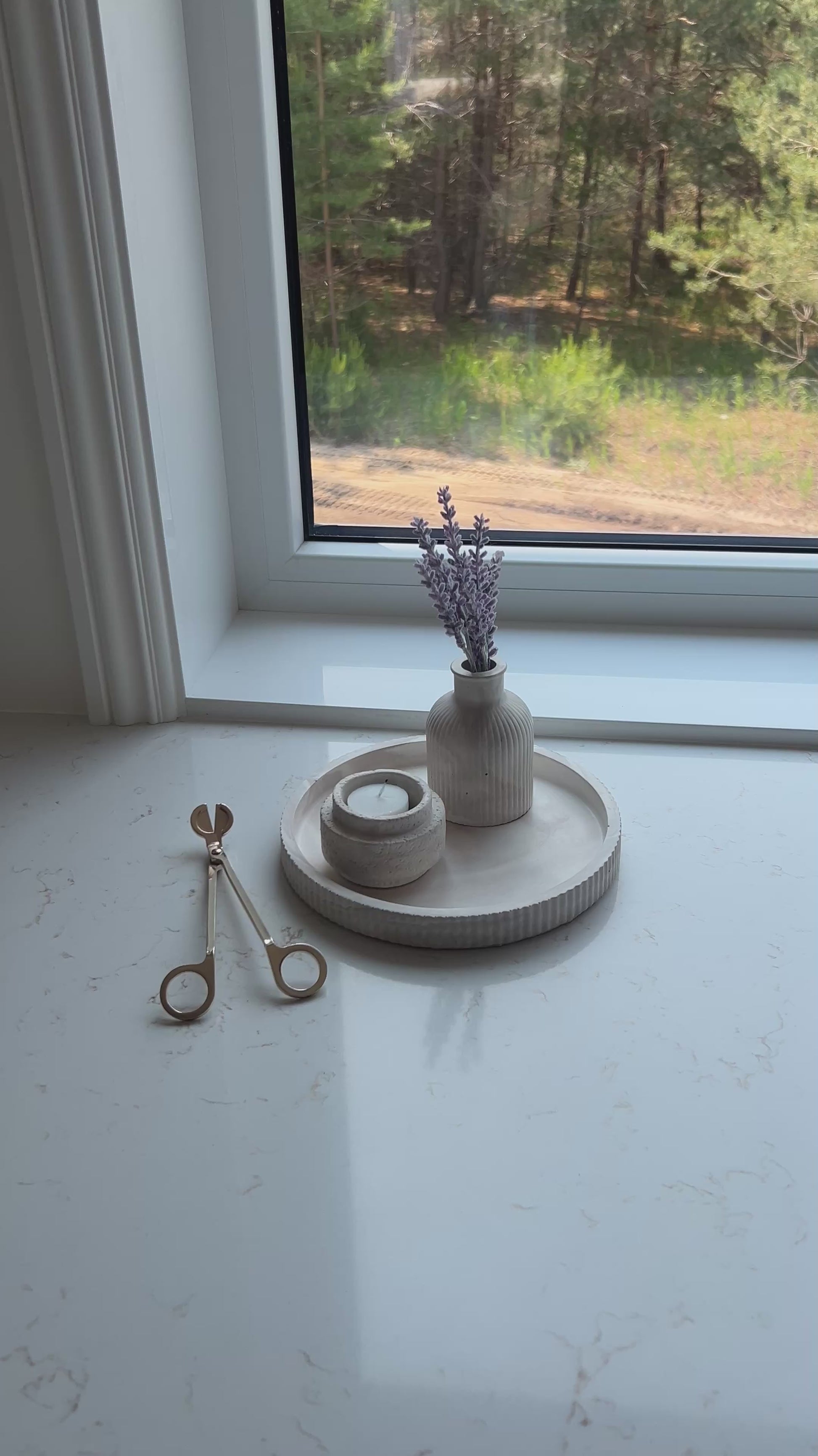 Video of our round limestone tray with a candle holder and budvase decorated on a marble countertop in front of a window 