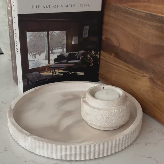 Round limestone tray with candle holder on a kitchen countertop with a book and wooden cutting board 