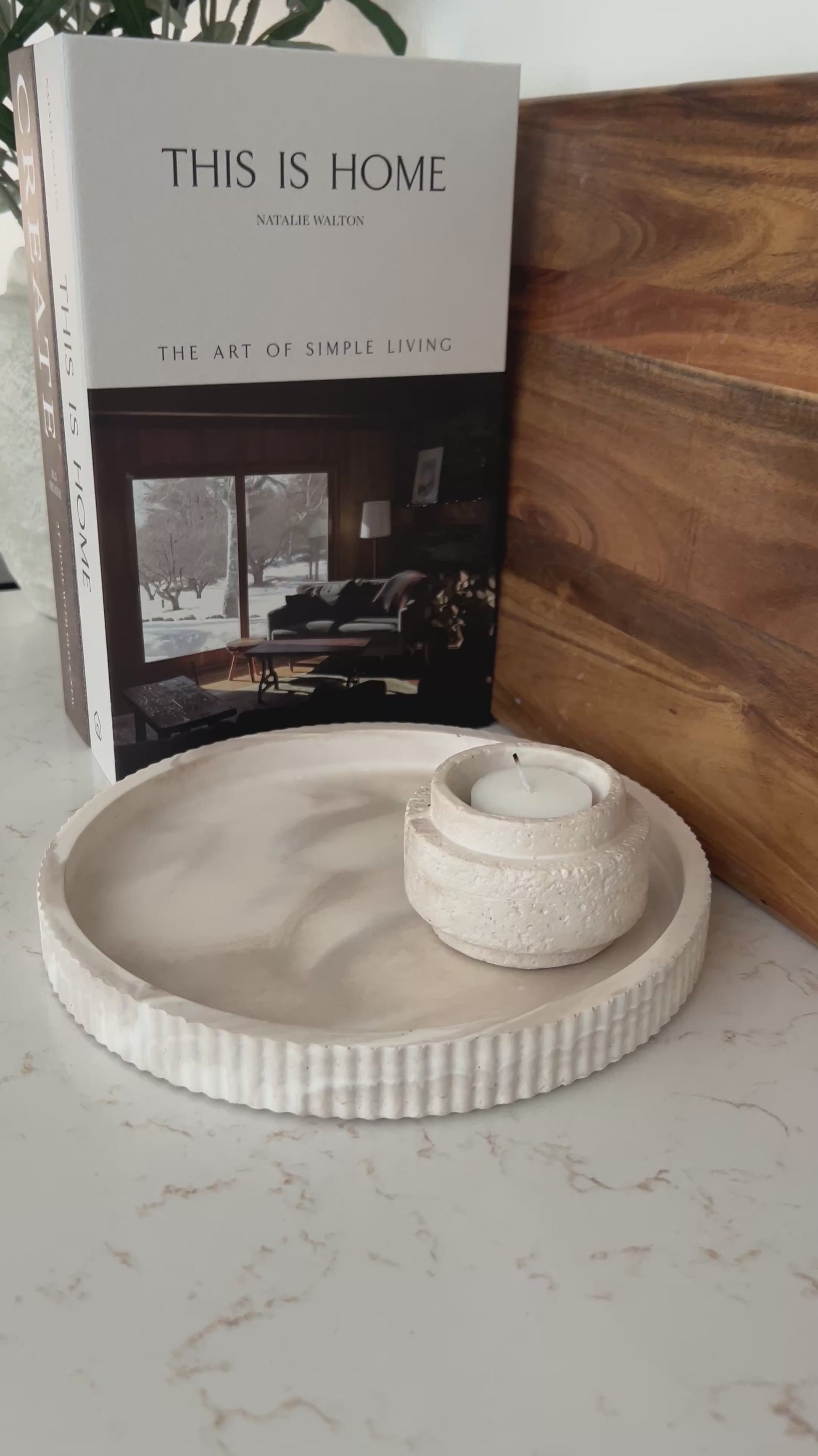 Round limestone tray with candle holder on a kitchen countertop with a book and wooden cutting board 